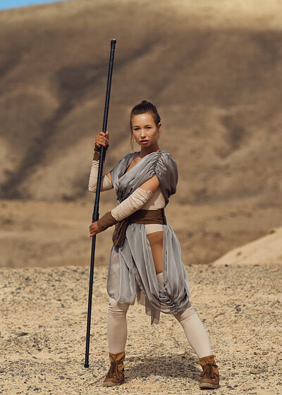 Big-chested beauty strikes a pose while dressed up as a Star Wars character, showing off her wares and attending to a strong companion amidst sandy terrain.