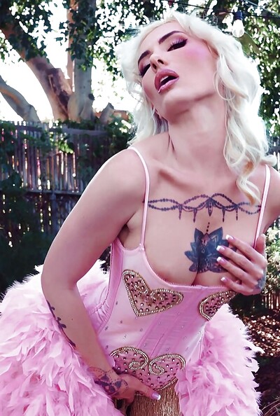 Platinum curls frame her daring gaze as her inked skin and confident curves contrast the softness of her ensemble.