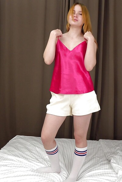 The playful ginger teen, now nude after removing her shorts, silk blouse, and knee-socks, rubs her shaved pussy and clit.