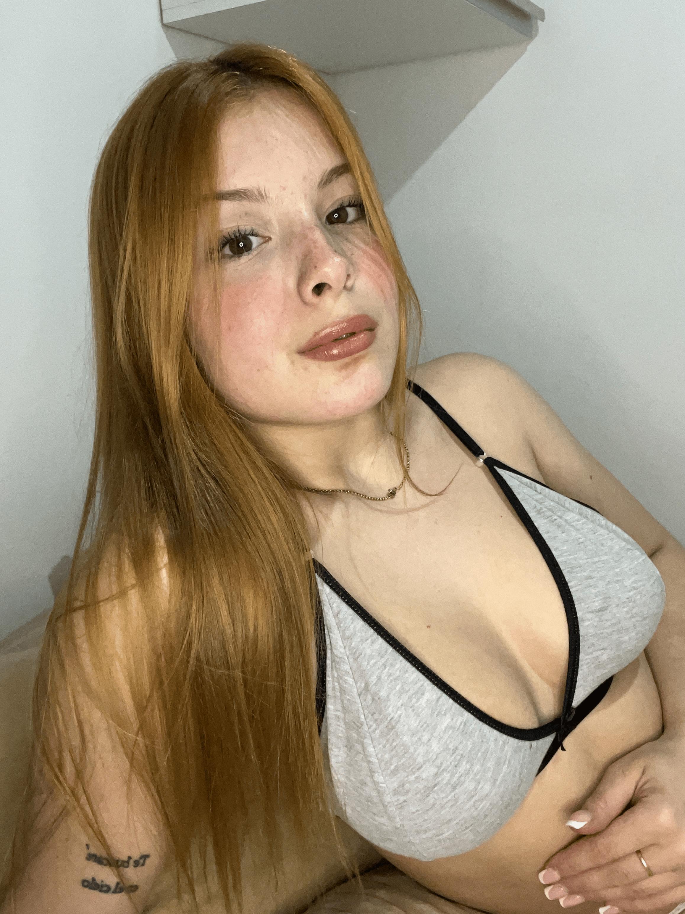 Mia Prescott's red hair cascades as she gazes seductively, her hand teasing her cleavage, lips slightly parted.