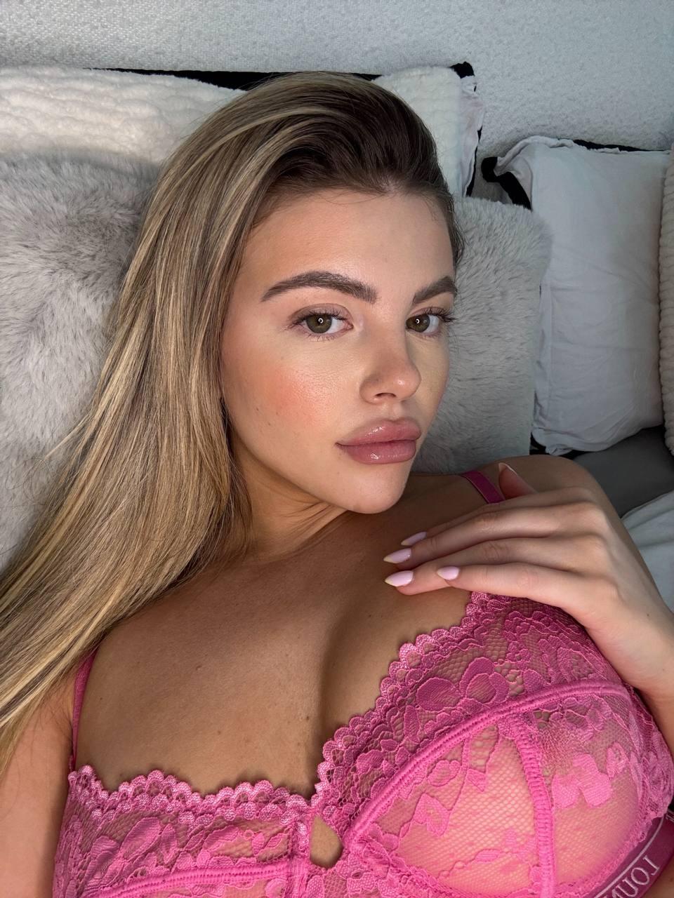 Tilly Harrington's lace bra is teasing with its sheer pink fabric, her hand resting on her chest.