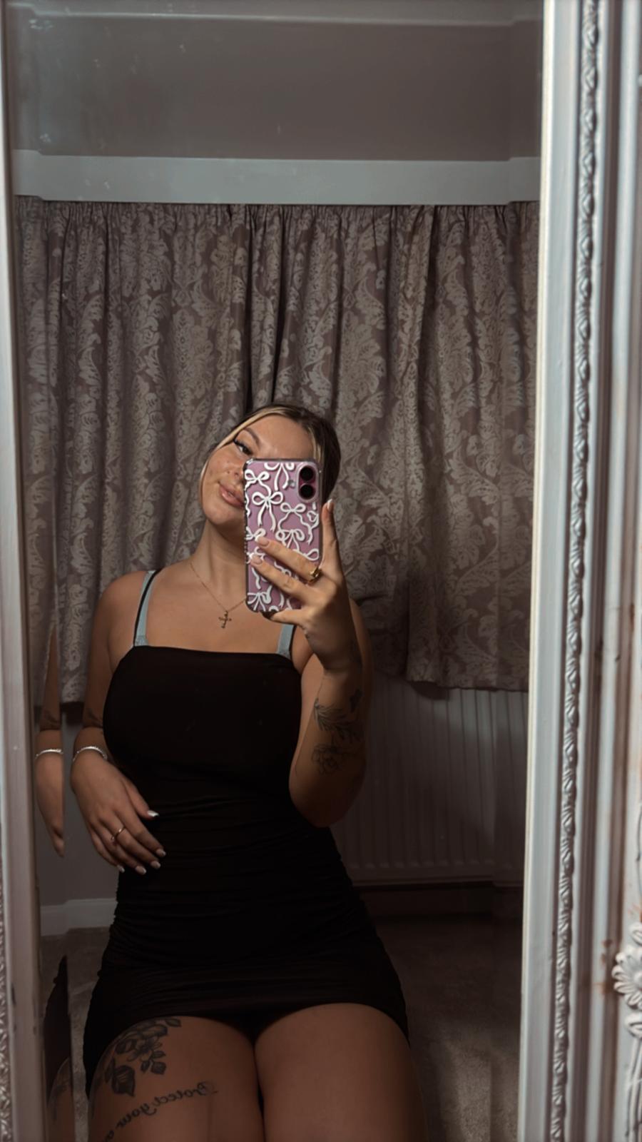 Sofia Bae's tight black dress hugs her curves, her hand on her thigh, anticipating your touch.