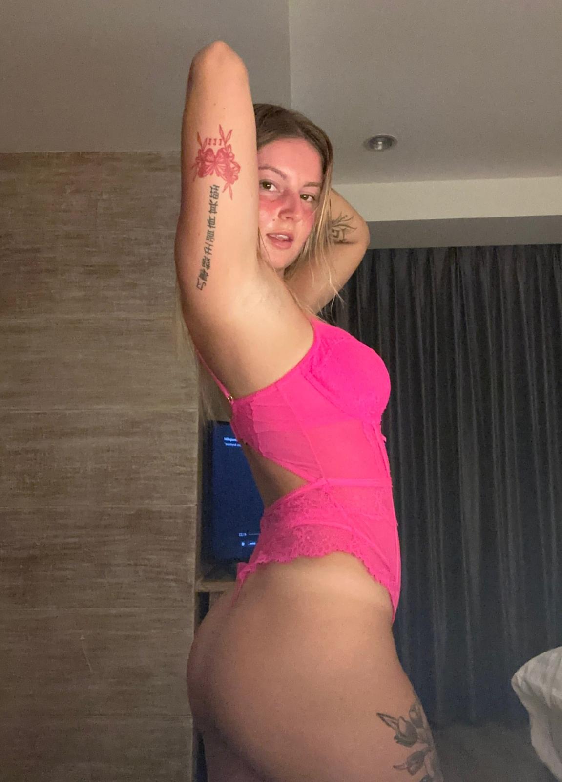 Sofia Bae's pink lace lingerie hugs her curves, her arms raised, revealing a tattoo, and her ass is ready.