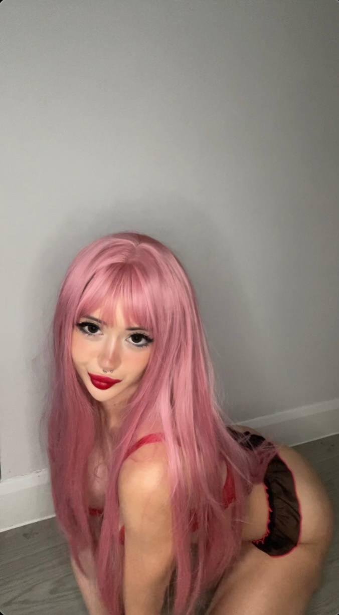 Mimi's pink hair frames her face as she kneels, her red lips parted, anticipating your touch.