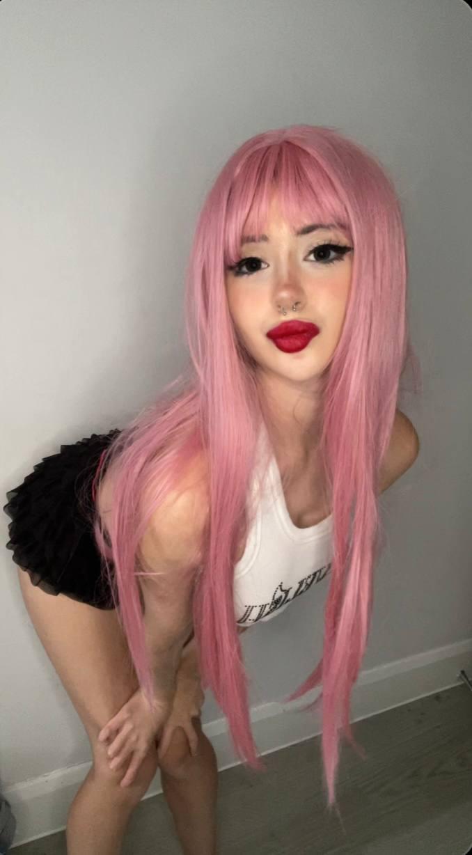 Mimi's pink hair cascades as she bends forward, her red lips parted in anticipation, hands on her thighs.