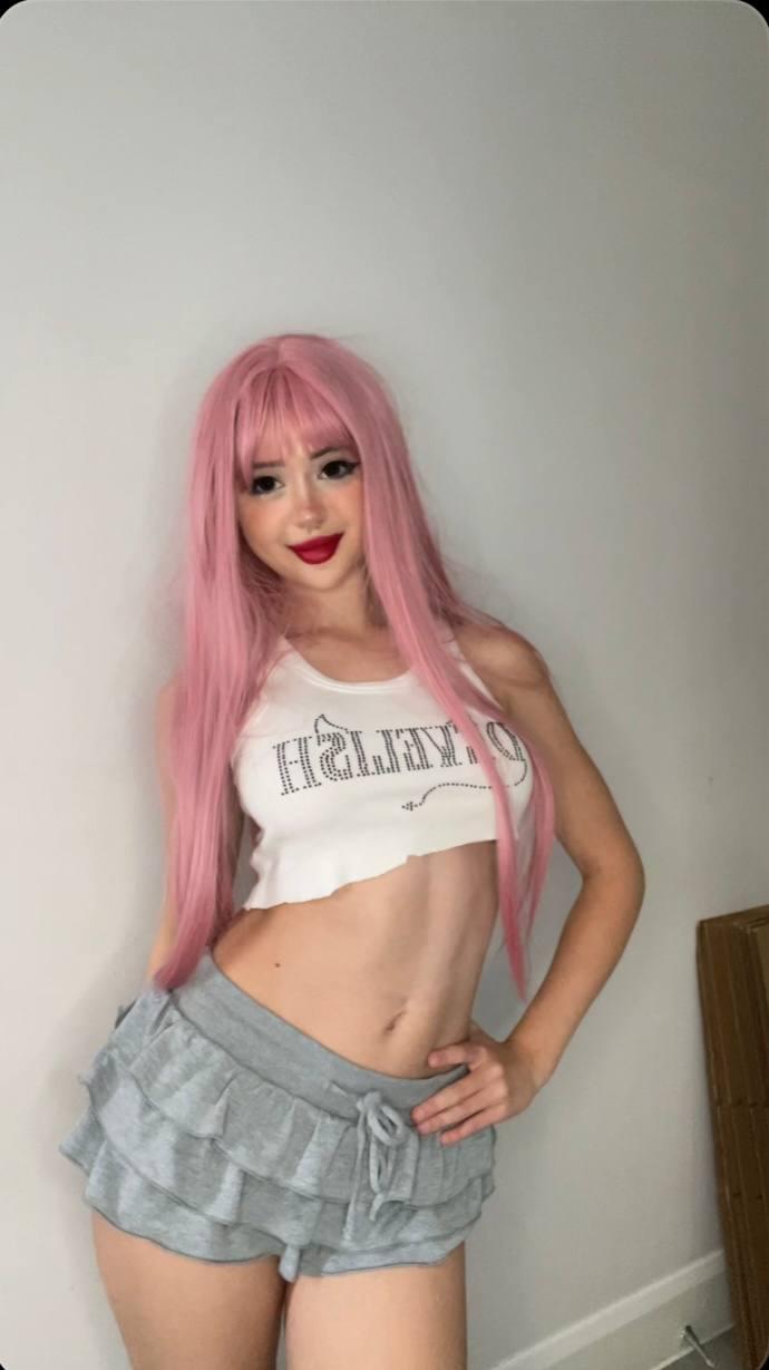 Mimi's pink hair frames her face as she teases, her hand on her ruffled shorts, her midriff exposed.