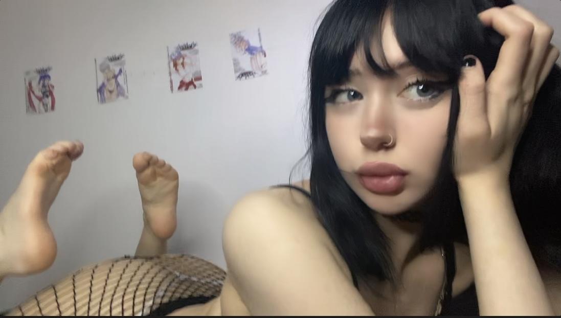 Mimi's sultry gaze, black fishnet stockings, and soft lips tease, feet up, wall art in the background.