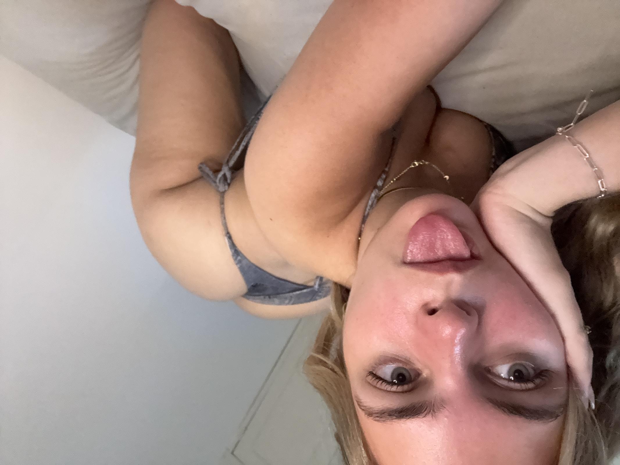 Ellie Rose's tongue teasingly touches her lips, her wet pussy barely covered by denim shorts, anticipating a deep kiss.