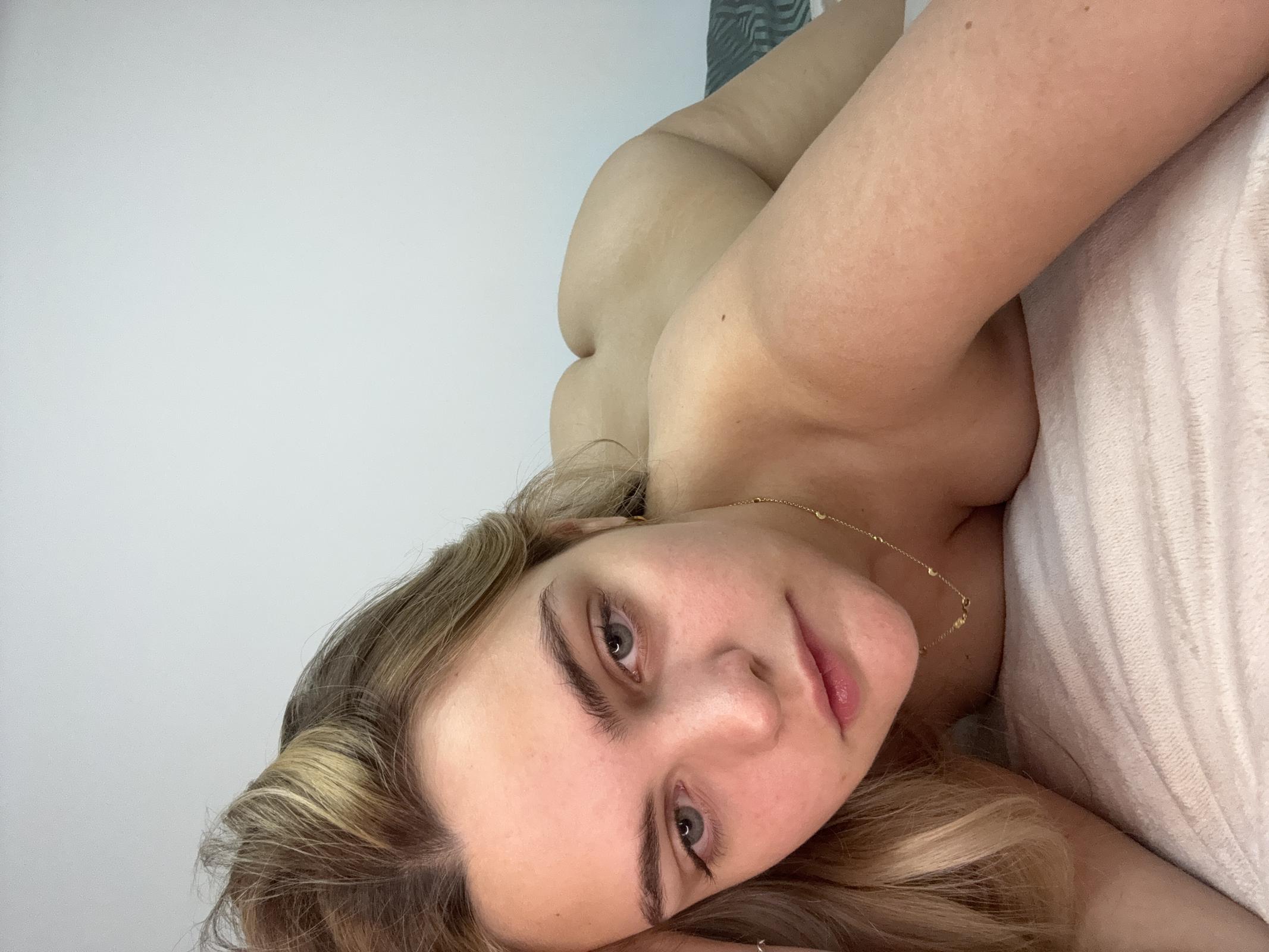 Ellie Rose's bare shoulder and golden necklace tease, her eyes half-lidded in sensual anticipation.