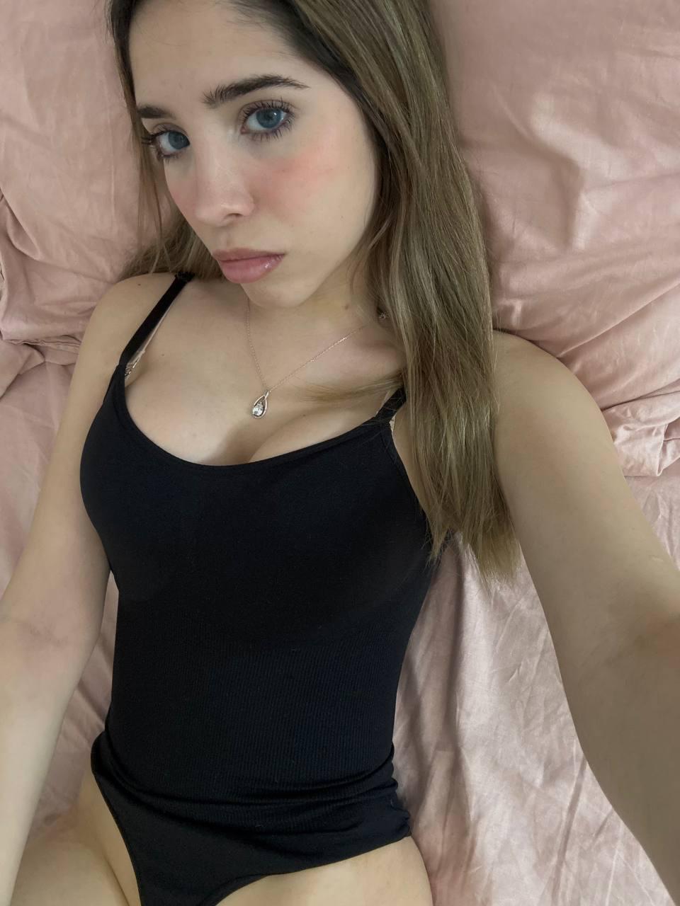 Ella's black tank top hugs her curves, her flushed cheeks hint at her growing arousal.