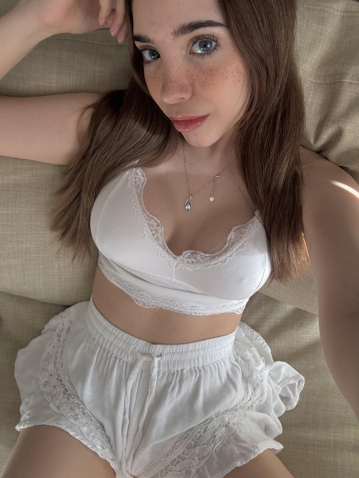 Ella's freckled face is flushed, her white lace lingerie teasing, her hand resting on her thigh.