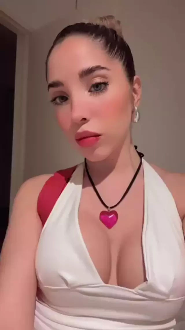 Ella's plump lips are slightly parted, her cleavage teasing, heart necklace drawing eyes to her chest.