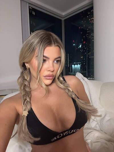 Tilly Harrington's braided hair frames her cleavage, her nipples pressing against her black sports bra, city lights glowing.