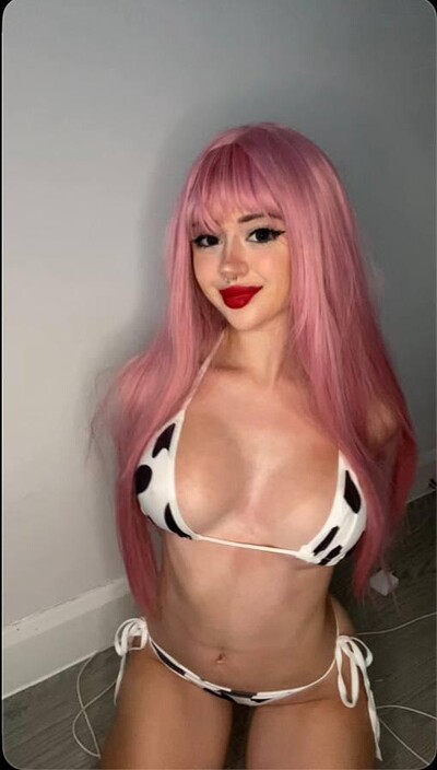 Mimi's pink hair frames her face as she kneels, wearing a cow-print bikini, her red lips slightly parted.