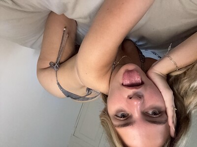Ellie Rose's tongue teasingly touches her lips, her hand on her cheek, her gray thong barely covering her ass.