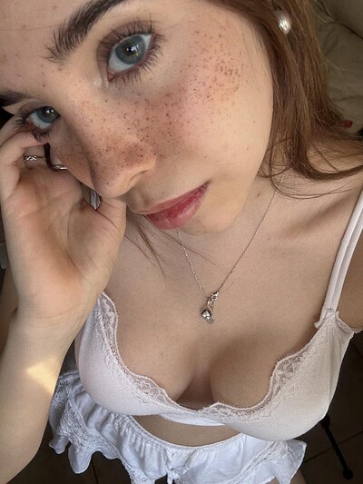 Ella's freckled face gazes up, her hand touching her ear, her cleavage inviting, her necklace glinting seductively.