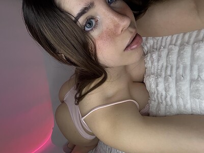 Ella's blue eyes lock onto the camera, her lips slightly parted, her pink lingerie barely covering her curvy ass.